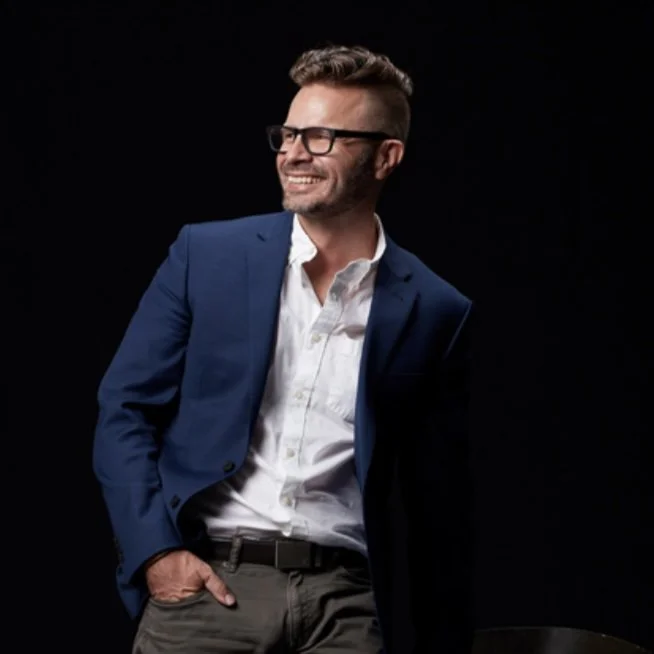 Jimmy, founder of Combustible Co., laughing in a blue blazer against a black background